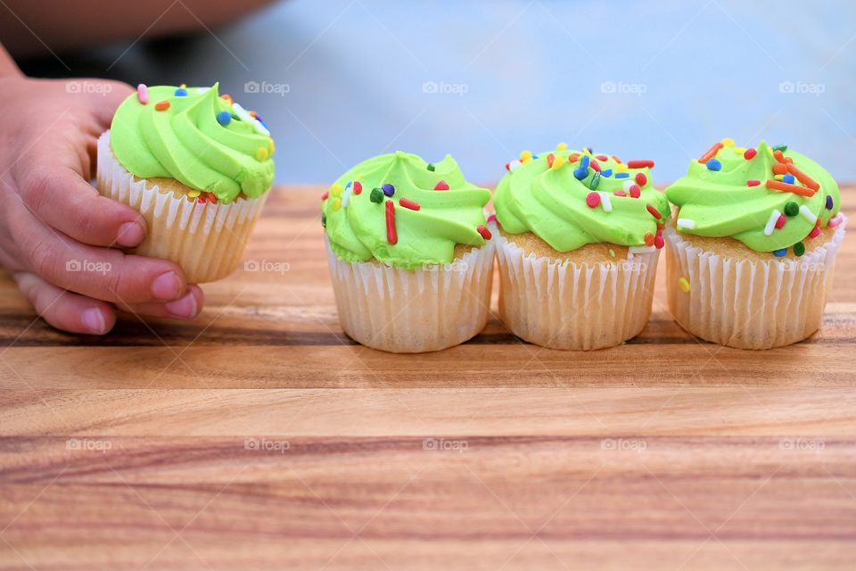 Indoor shot of toddle stealing a cupcake with vanilla cupcakes with the colorful icing with sprinkles 