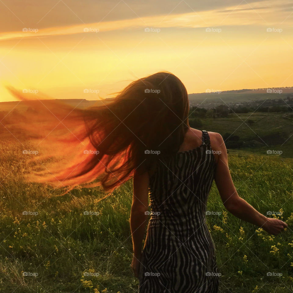 Young woman catching the sunrise light by her long hair in the summer field 