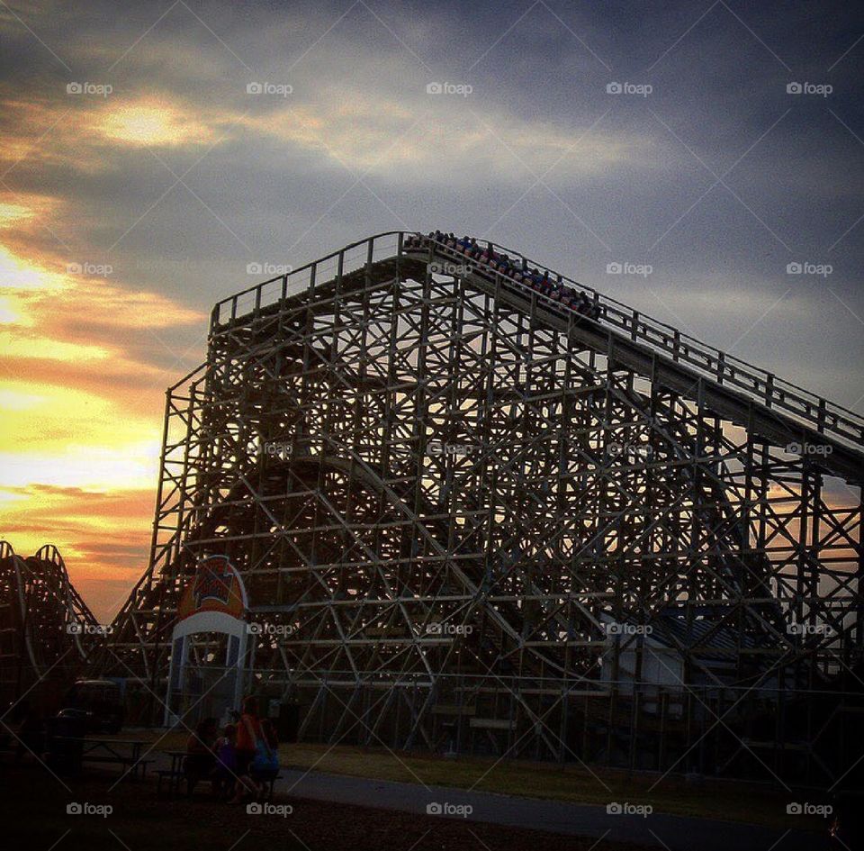 Wooden roller coaster in cloudy sunset.