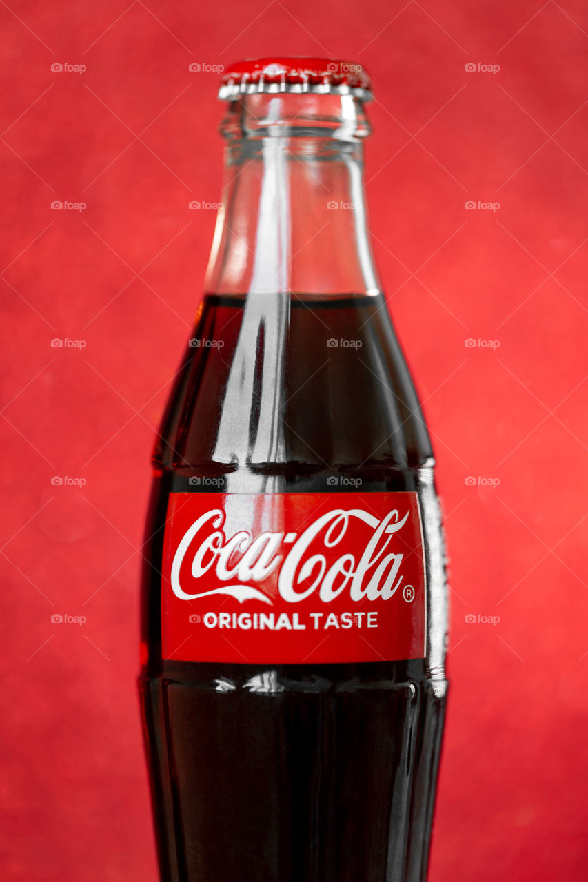 Coca-Cola glass bottle on red glitter background, closeup