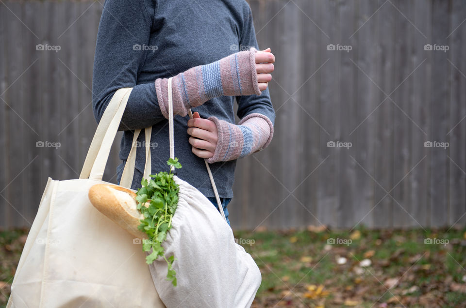 Millennial woman wearing fingerless gloves and carrying reusable grocery bags outdoors in the fall