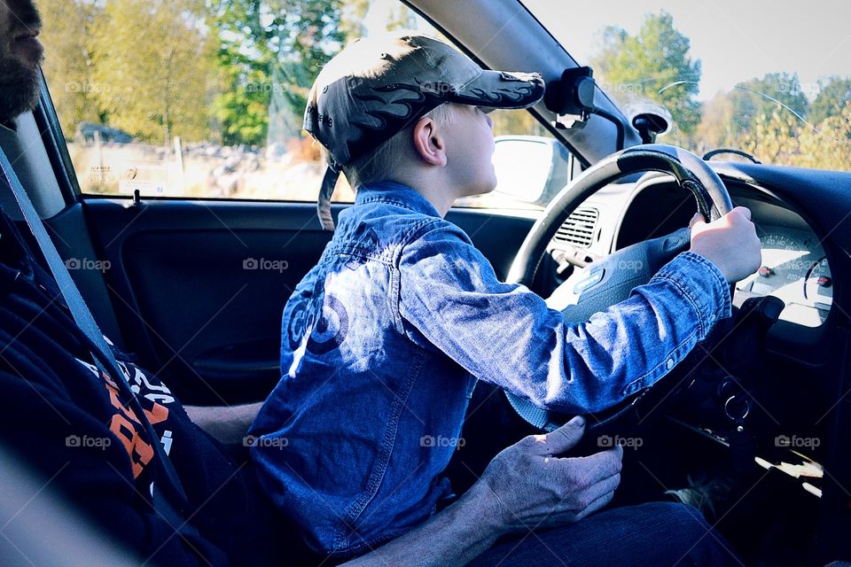 Boy playing with a syeering wheel in his fathers lap