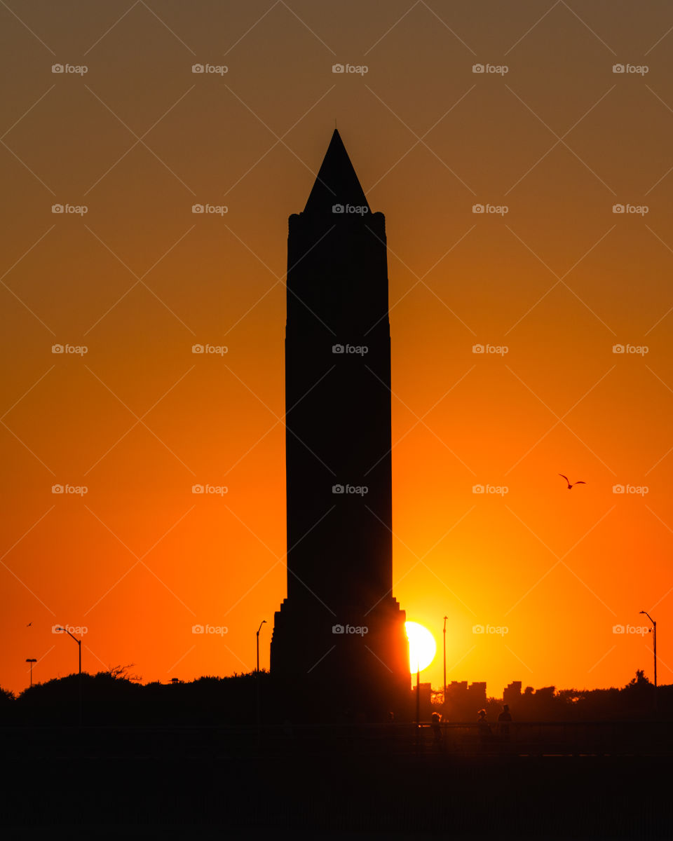 Silhouette of a large water tower as the sun sets behind it - vibrant orange sky.