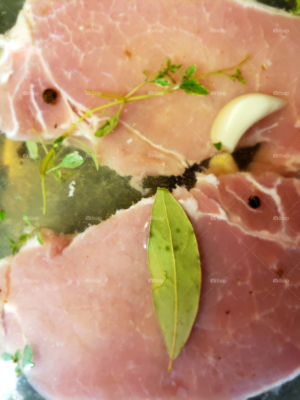 Pork chops marinating with herb leaves and garlic slices.