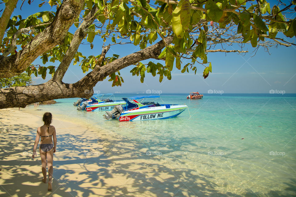 Follow me to the sea. girl walking on the beach towards a speed boat during a hot sunny day