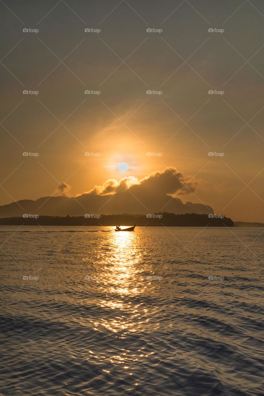 Sunrise above silhouette of boat in sea