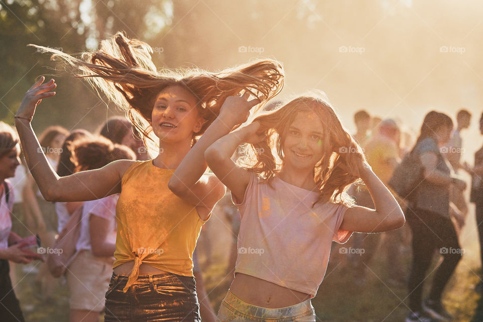 Portrait of happy smiling young girls with colorful paints on faces and clothes. Two friends spending time on holi color festival