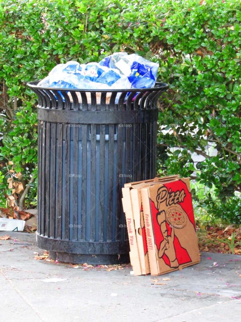 pizza boxes sitting by a black trash can that is full of trash
