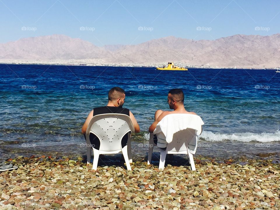 Rear view of men sitting on chair in front of sea