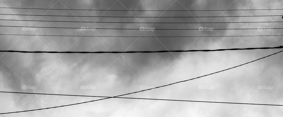 parallel electricity cables with cloudy sky as a background