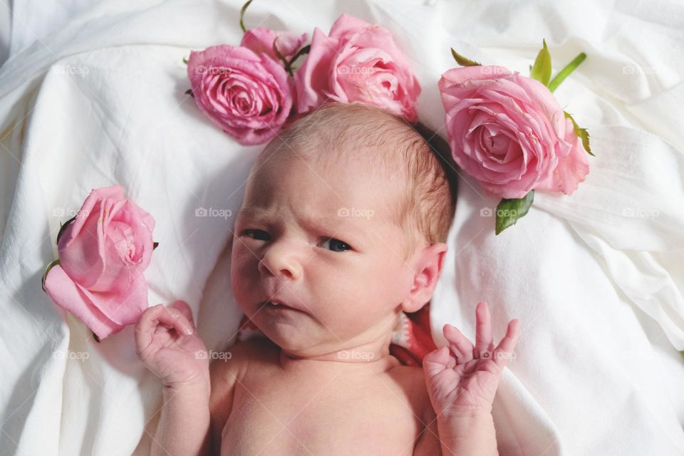 Dissatisfied newborn lies on white sheets with roses