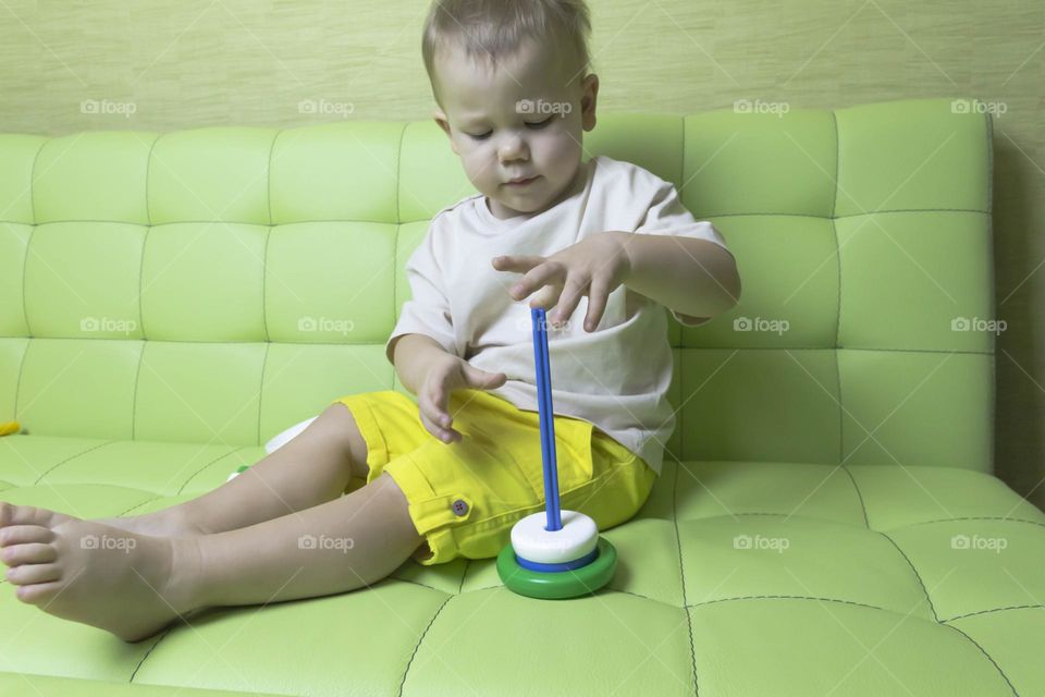 The child is having fun playing a bright pyramid educational toy, sitting on a green sofa.