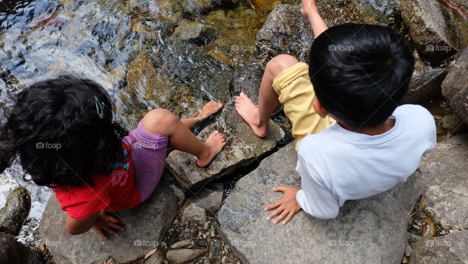 Childhood friends dipping bare feet in river water during summer trip.