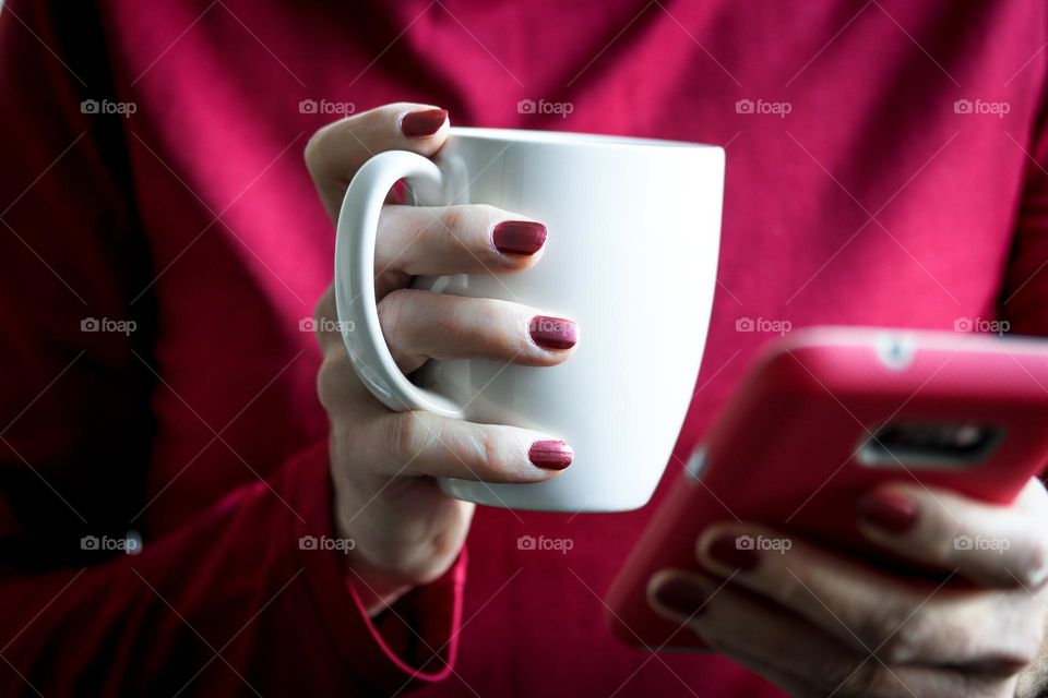 Viva magenta: lady's hands with simple magenta manicure are holding cup and a cell phone