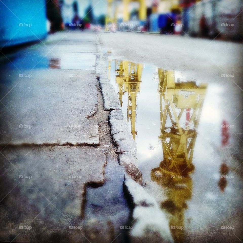 Industrial cranes are reflected in a puddle on the streets of a Gdansk shipyard.  