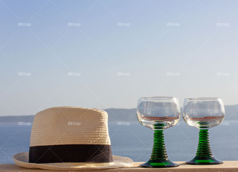 Summer still life.  A sunny day, a hat and two glasses of wine on the railing of the terrace overlooking the warm calm sea.  Summer holiday attributes