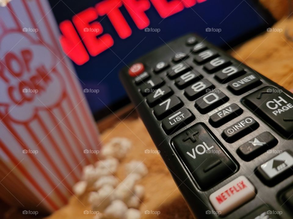 Aiming the remote control at television screen to choose favorite netflix channel to binge watch TV shows or movies for a fun and cozy night in with a popcorn snack