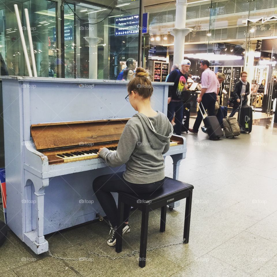 A teen girl playing a piano at the St-Pancras international train station. 