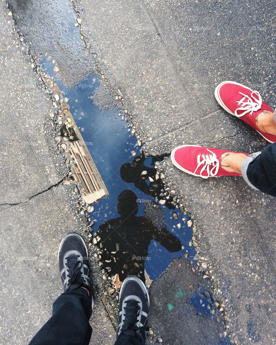 Two people staring into a puddle on the street. 