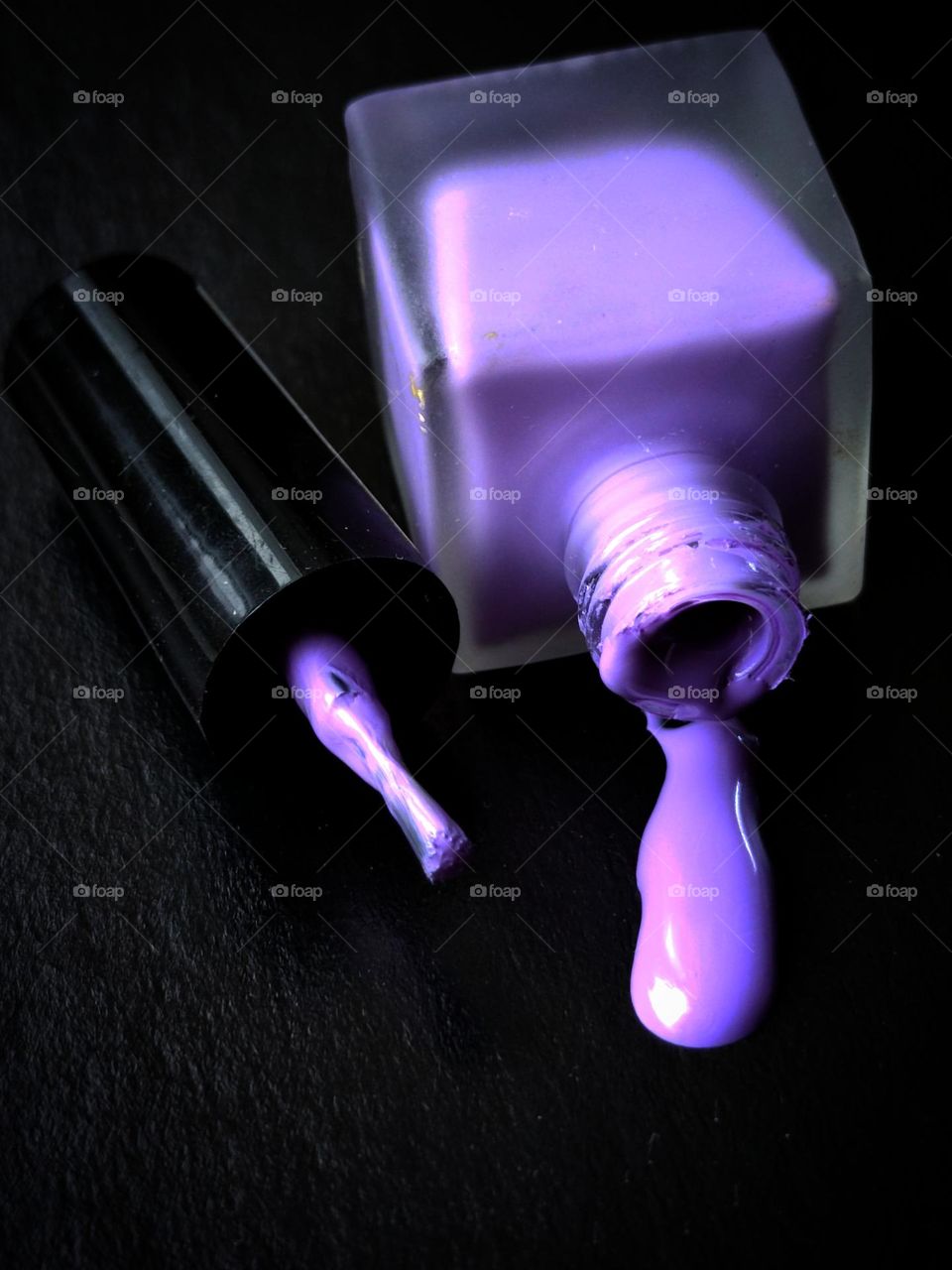 An overturned nail polish bottle, leaking purple nail polish, and a brush with purple nail polish residue. Black background