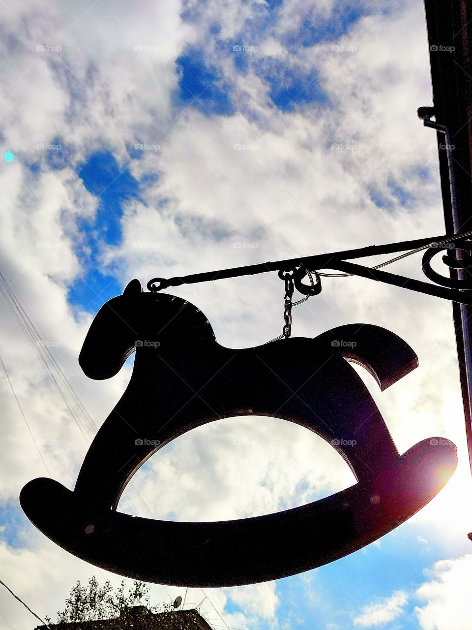 Toy store decor.  A small wooden horse is suspended from the house.  In the background blue sky with white clouds and sun