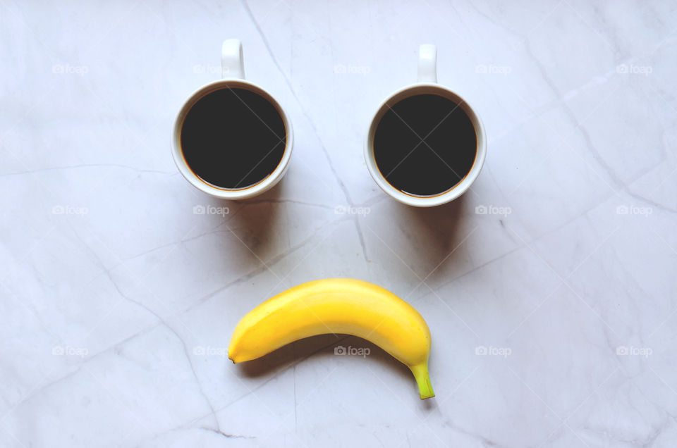 Business working morning with cup of hot coffee and yellow banana on white background close up. Game of noughts and crosses. Top view, copy space, flat lay, mockup. Sad emotions.