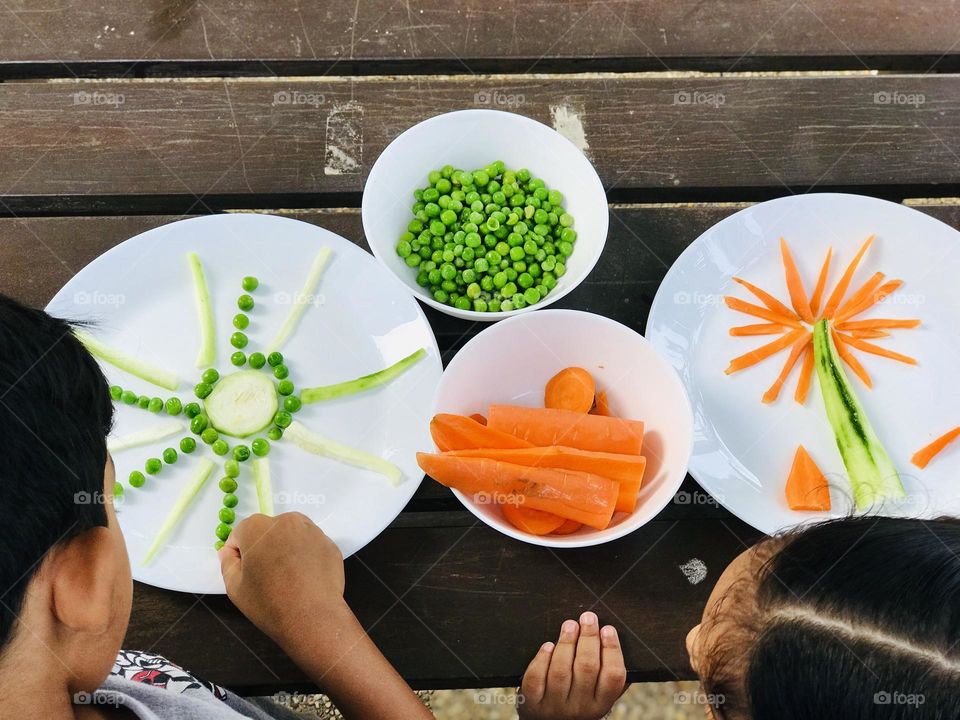 Kids enjoying by doing creative activities with vegetables. They are making sun and coconut tree with greenpeas  carrots.