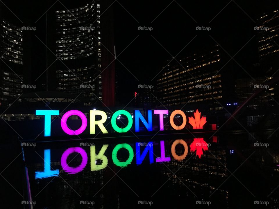 The Toronto sign lit up at night surrounded by the bright lights of apartments.
