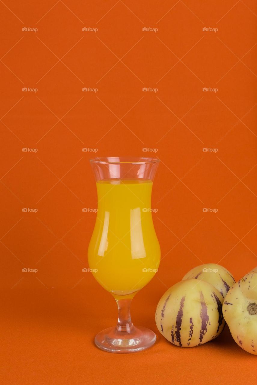 Cucumber and glass with natural juice on orange colored background