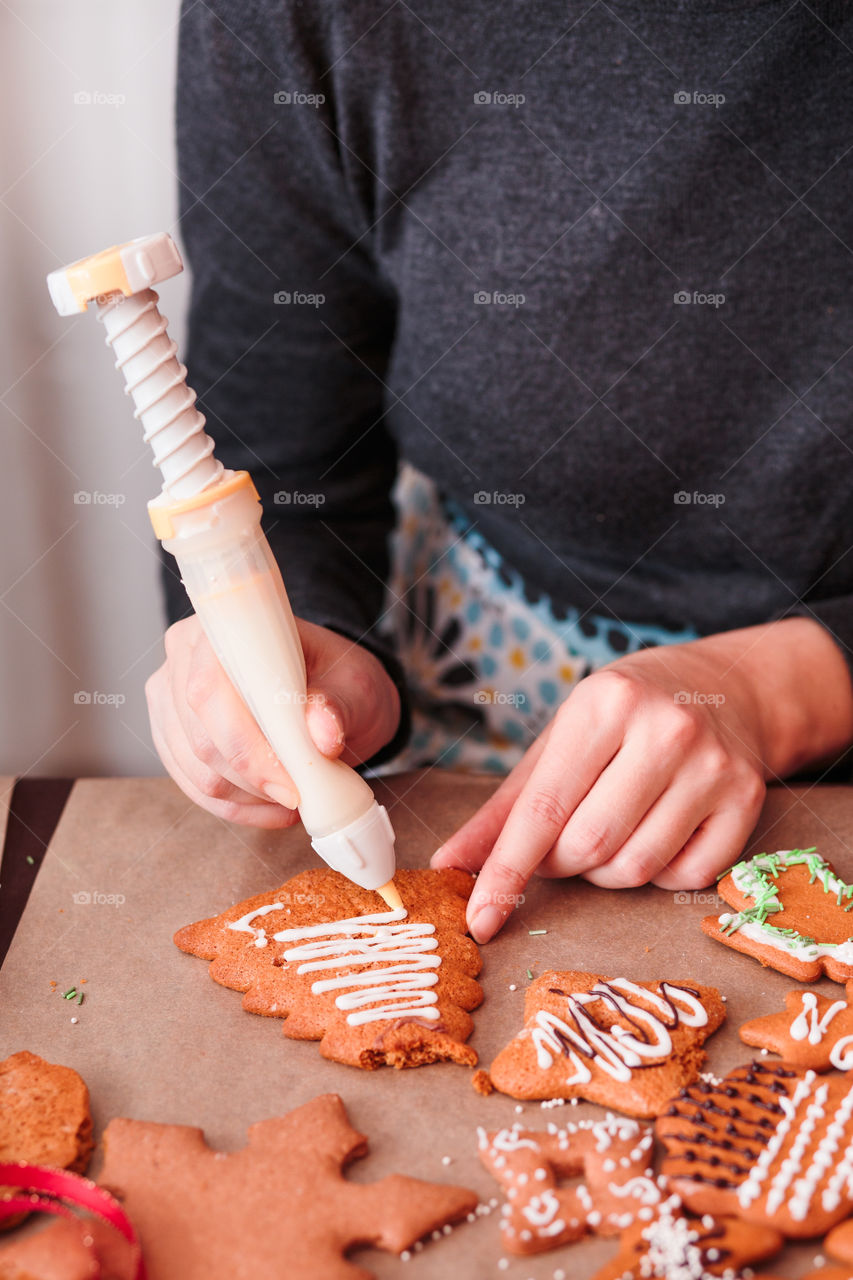Woman decorating baked Christmas gingerbread cookies with frosting
