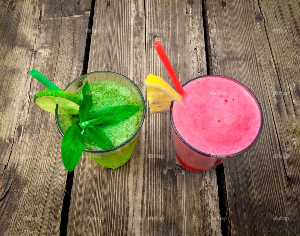 Two glasses with colorful red and green smoothies on wooden table