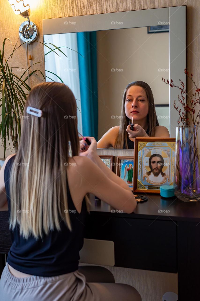 Home beauty salon woman paints her lips looking in the mirror