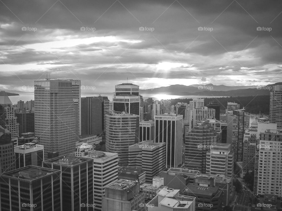 This cityscape is more dramatic in B&W. The photo is more dynamic due to contrasting: windows & building frames; sun shine peaking through dark clouds and ; sunbeam reflecting on the water. ☁️