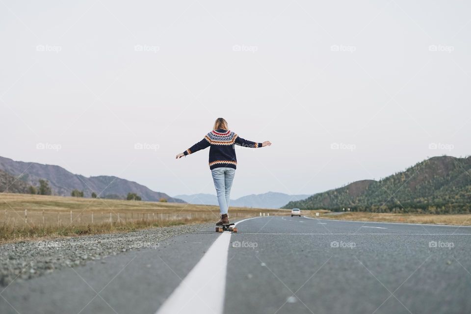 Young woman on skateboard on road against beautiful mountain landscape