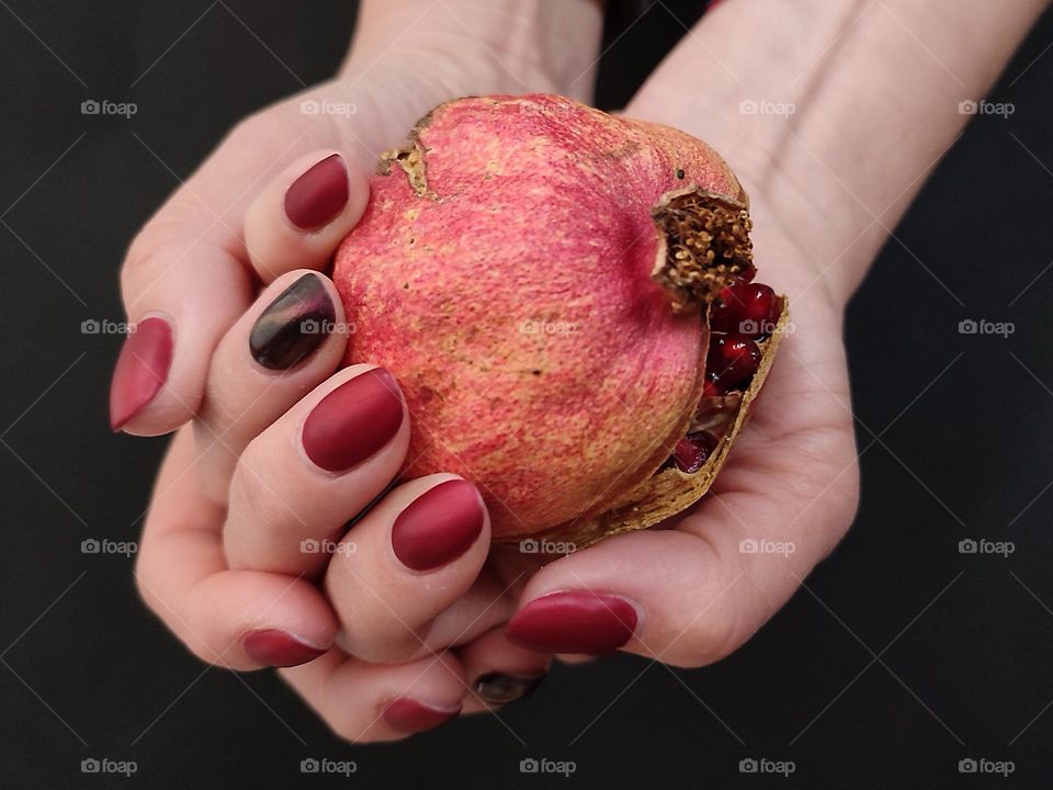 Beautiful female hands with nice art manicure holding a ripe pomegranate