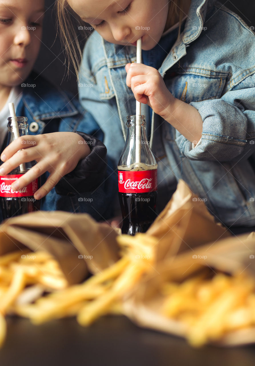 beautiful brother and sister of Caucasian nationality, at home, drinking Coca-Cola, laughing, rejoicing, hugging and having fun.  Happy kids dressed in denim clothes.  beautiful advertisement.  Lifestyle photo