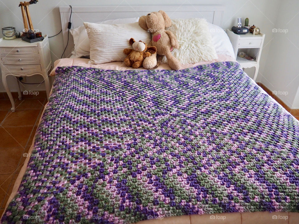 Shades of purple hand made crochet blanket on girl’s bed.