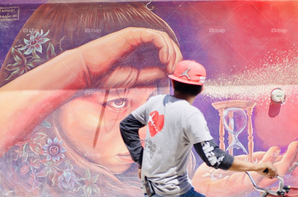 Perfect timing. A girl in a street art mural seems to taking a man’s hat who is passing by on a bike.