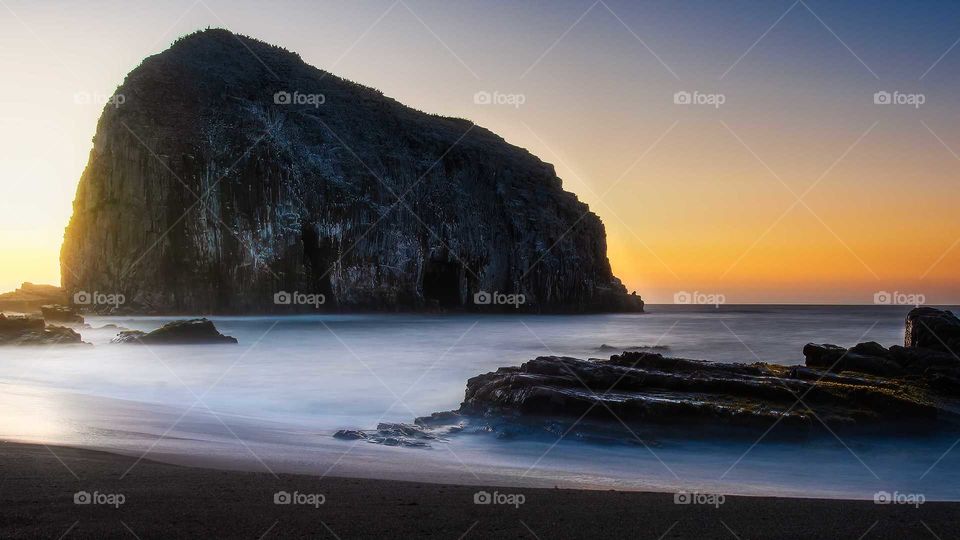 view of the coast in long exposure, in the background a rock giants