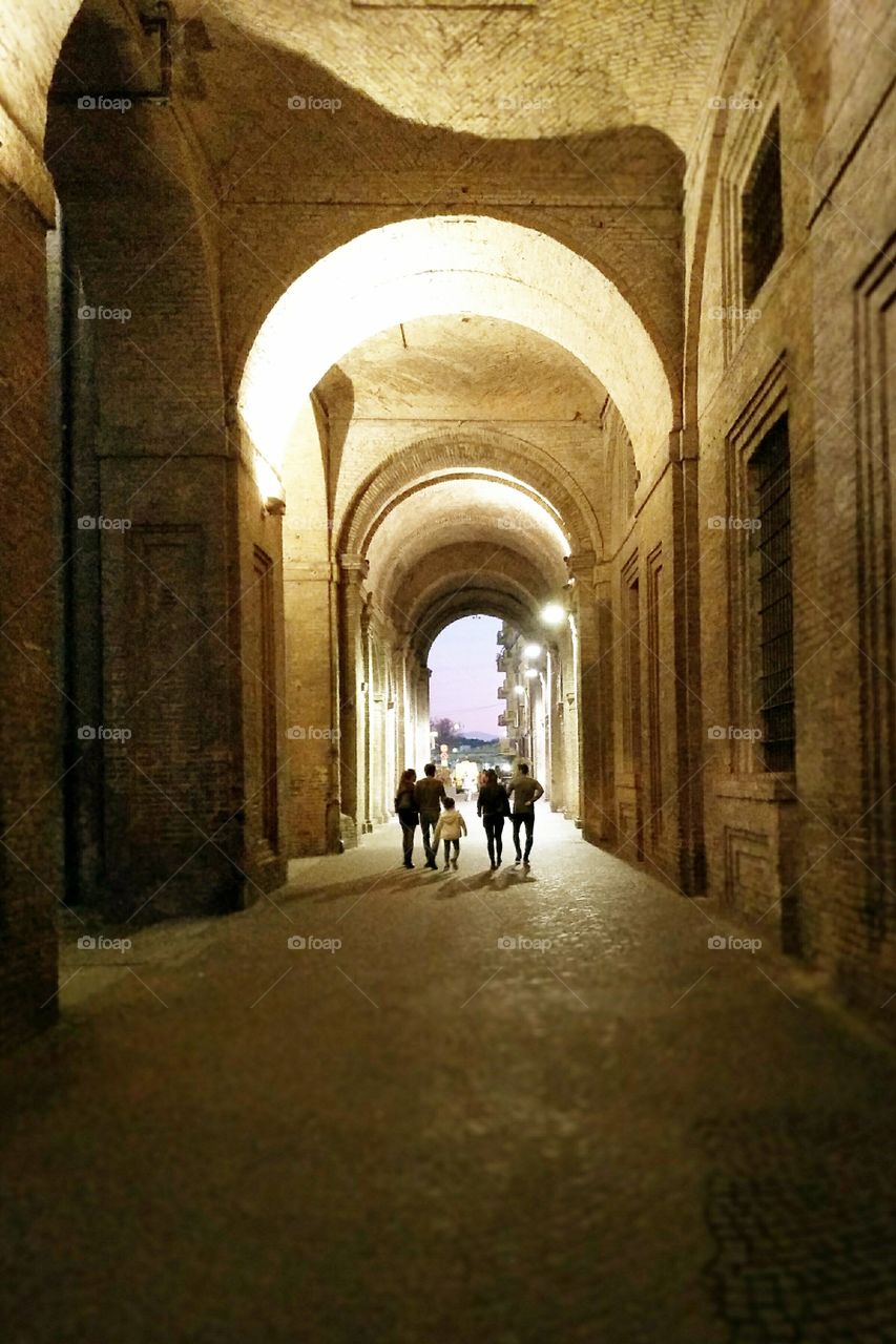 some people walk towards the exit of a gallery of an ancient palace