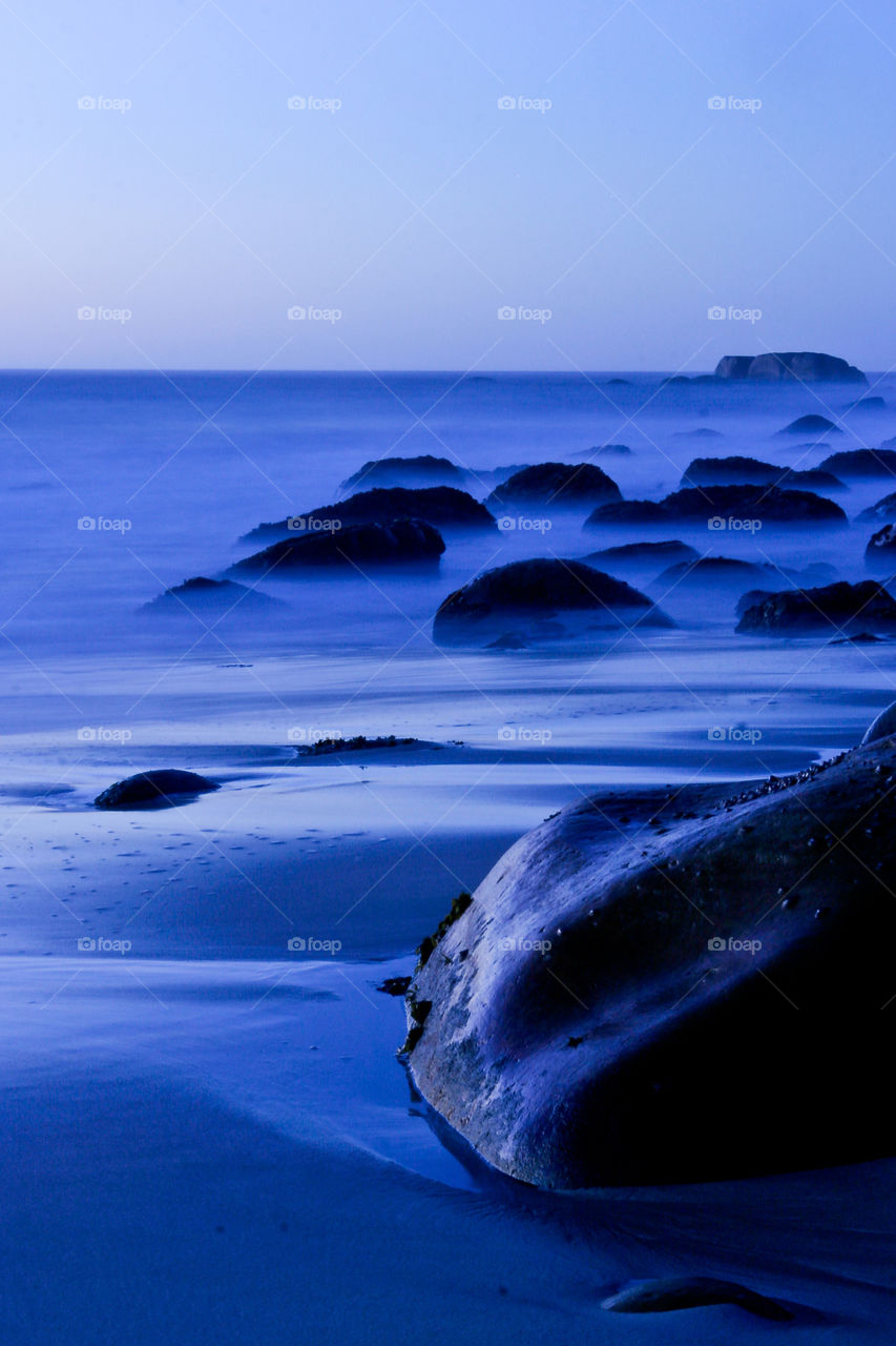 Night time over boulder beach with mist and fog rising over the ocean. Large rocks on the sea shore.