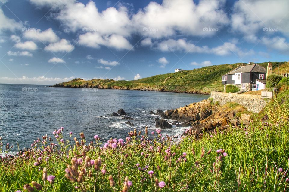 Seaside House. A Cornish Country Cottage sits at the edge of the ocean with a beautiful views of a bay. Bright sunny day.