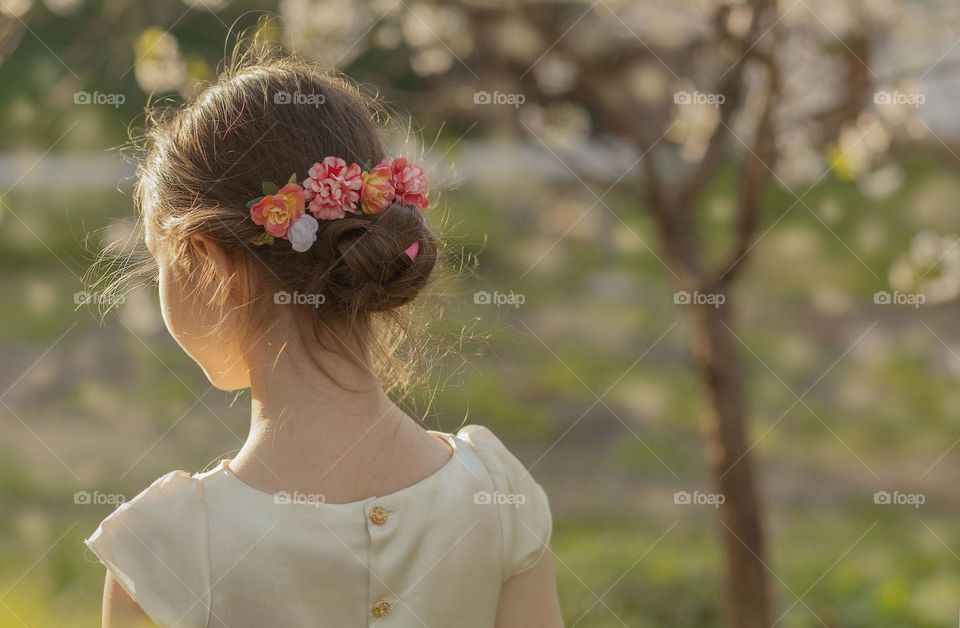 Portrait of a girl from the back against a background of cherry blossoms, a beautiful hairstyle in the sun.

￼