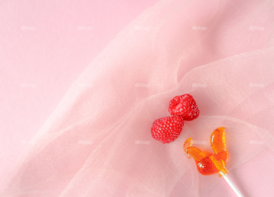 Romantic photo with a two raspberries and a lollipop on a light pink background . Easy, tasty snack girl. The concept of Valentine's day. Food photos, top view, copy space