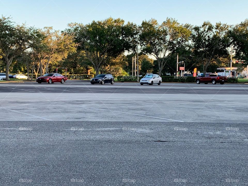 Commuting: cars, vehicles parked and ready to come in or leave in a parking lot and street by trees.