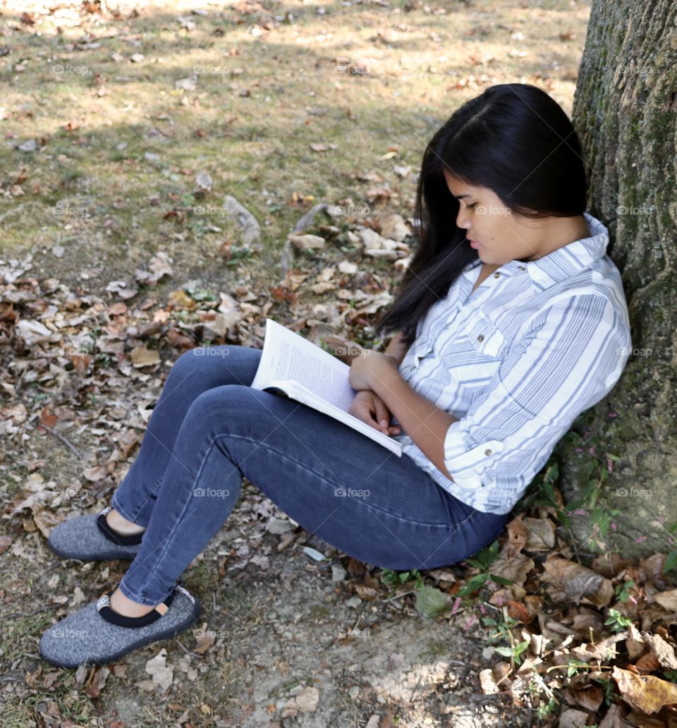 Relaxing while sitting under a tree reading a book 