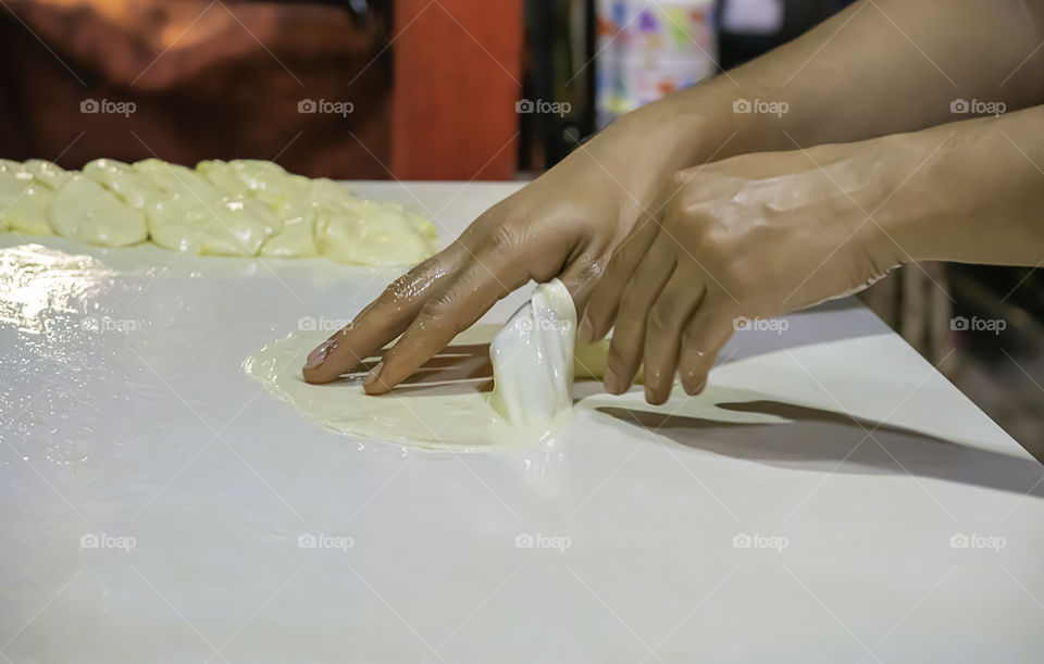 Hands kneading dough to a sheet on the table.