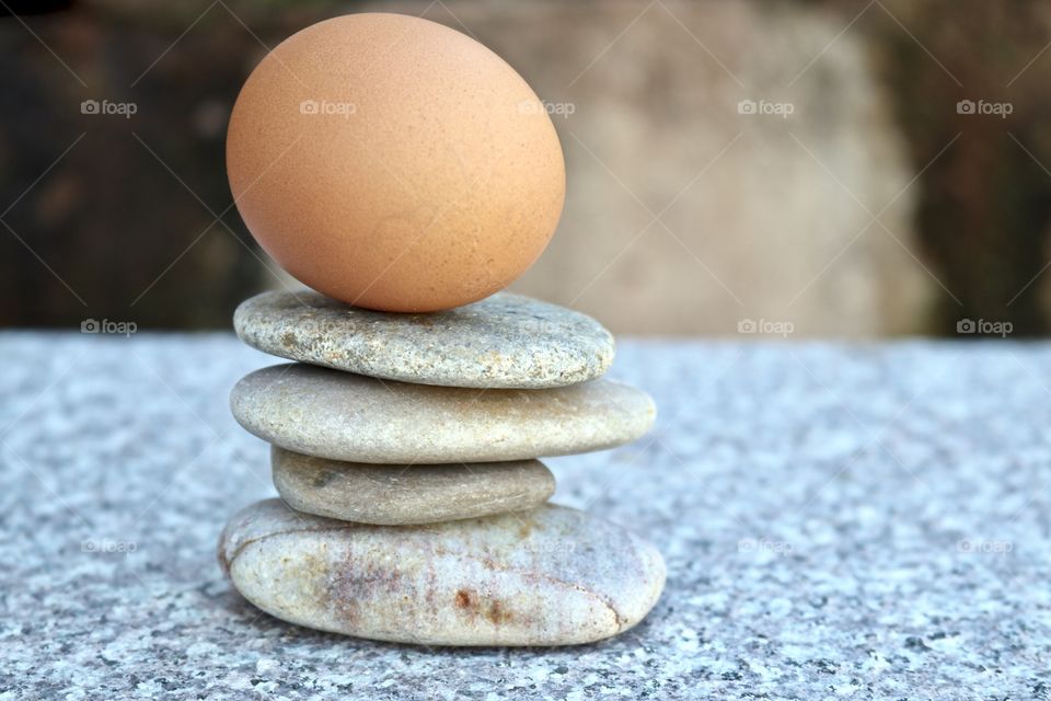 Brown egg balancing atop smooth stone rock stack on marble surface, concept life, business, ideas, creativity endurance or stability