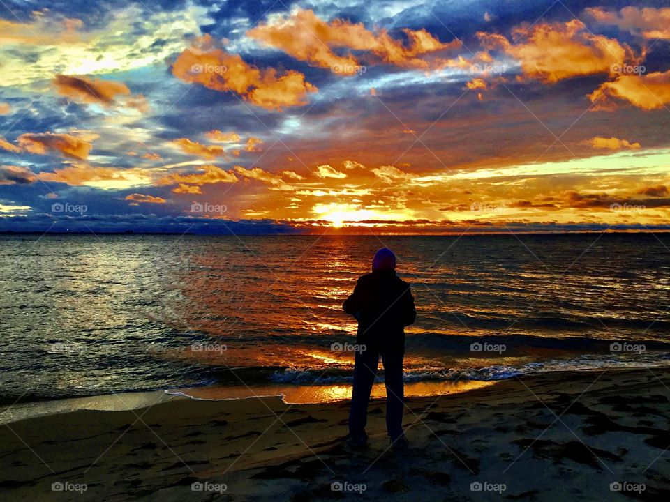 Silhouettes and shadows - A silhouetted woman gazes at an colorful and explosive sunset as orange clouds float by and the waves crash the sandy beach