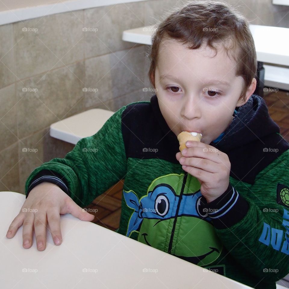 A little boy gets serious about eating his vanilla ice cream cone. 